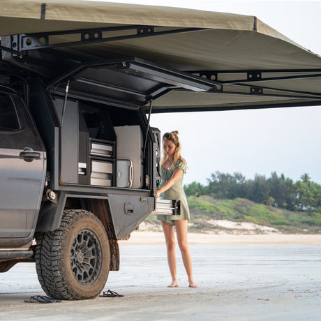 Person standing next to a vehicle with aBush Company 270 XT MAX Awning  on a beach.