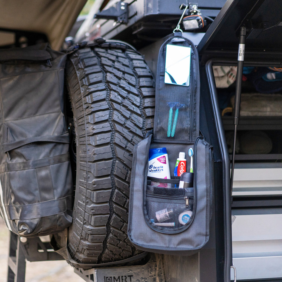 Compact wash bag hung open from a 4WD rear door beside the spare wheel, packed with toiletries