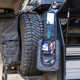 Compact wash bag hung open from a 4WD rear door beside the spare wheel, packed with toiletries