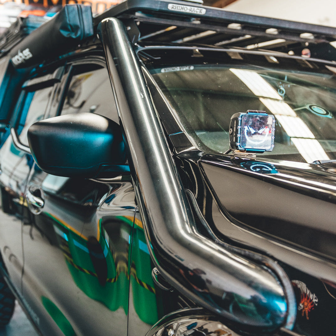 Close-up of a vehicle's side mirror and bumper with a reflective surface.