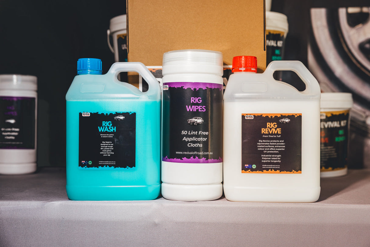 Three automotive care product containers on a shelf: a turquoise jug labeled Big Wash, a white canister labeled Rig Wipes, and a white jug labeled Rig Revive, with additional containers blurred in the background.