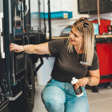 Woman in a garage holding a bottle, with a vehicle and tools in the background
